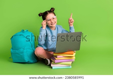 Full body photo of intelligent little girl wear blue pullover sit with laptop directing empty space isolated on green color background