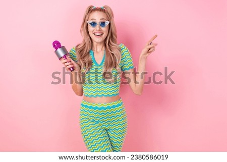 Photo of good mood impressed woman wear wavy blouse in sunglass hold microphone directing at empty space isolated on pink color background