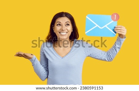 Funny embarrassed woman holding holding mail sign isolated on yellow background. Young casual woman holding blue paper envelope with number one and shrugs smiling. Banner. Email concept.