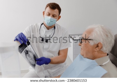 Good looking old man patient have a appointment at the dentist he sitting on the dentist chair and discussing with the doctor the problems of caries Royalty-Free Stock Photo #2380601153