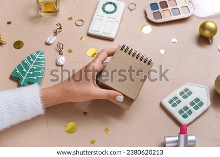 Woman with notebook, accessories, cookies and Christmas decor on beige background, closeup
