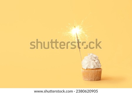 Tasty birthday cupcake with sparkler on orange background