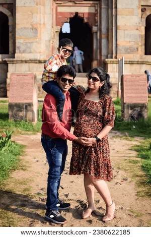 Indian couple posing for maternity baby shoot with their 5 year old kid. The couple is posing in a lawn with green grass and the woman is flaunting her baby bump in Lodhi Garden in New Delhi, India