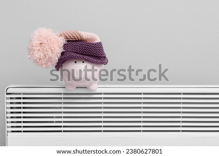 Piggy bank with hat on radiator near light wall. Winter heating concept
