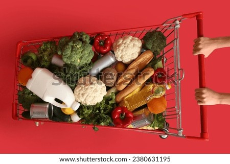 Woman pushing shopping cart full of food on red background Royalty-Free Stock Photo #2380631195
