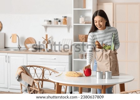 Young Asian woman unpacking fresh products from market at table in kitchen Royalty-Free Stock Photo #2380637809