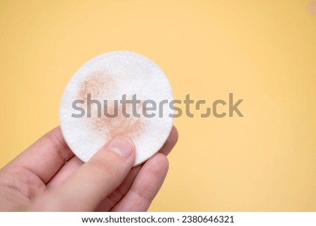 Girl holding a cotton pad in her hand, sponge for removing make-up, on yellow background. Foundation cream