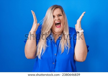 Caucasian plus size woman standing over blue background celebrating crazy and amazed for success with arms raised and open eyes screaming excited. winner concept 