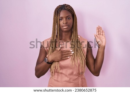 African american woman with braided hair standing over pink background swearing with hand on chest and open palm, making a loyalty promise oath 