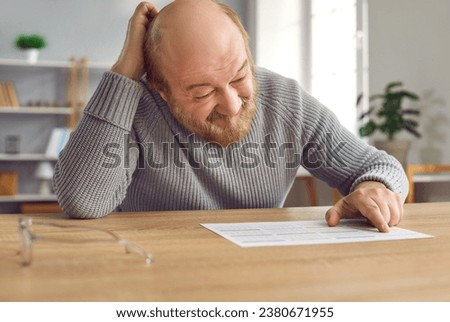 Senior man with dementia gets confused and scratches head when he looks at calendar on table. Old man with Alzheimer's disease can't remember important dates, events, birthdays, hospital appointments