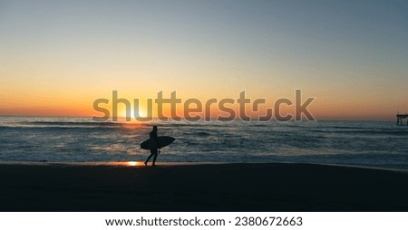 Surfer on beach in front of sunset 