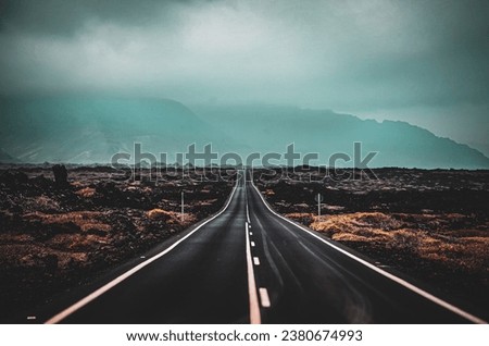 Long lonesome road running through a desolate landscape. Mountains in the background. Royalty-Free Stock Photo #2380674993