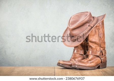 Vintage cowboy hat and old leather Wild West boots front concrete wall background. Retro style filtered photo
