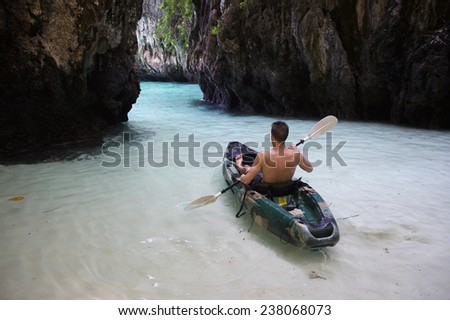 Young man kayaking through shallow tropical waters toward narrow rock cove
