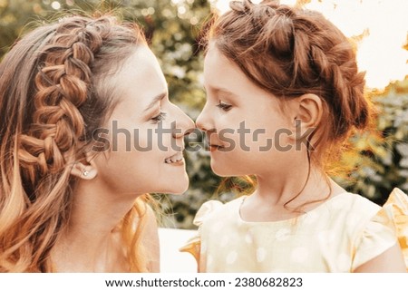 Maternity and loving motherhood. Beautiful young mom with braided hair hugging her lovely little sweet daughter while spending time together outdoors in garden under tree on summer day