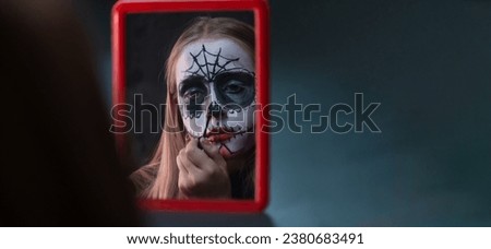 Young girl is painting skull on her face. Celebration of Mexico's Day of the Dead (El Dia de Muertos)
