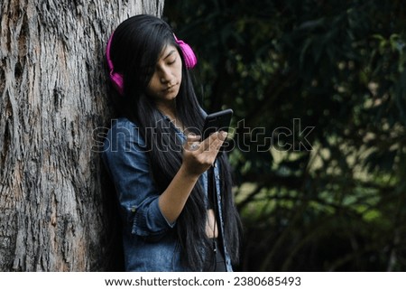 Attractive young woman with headphones enjoying music or a podcast in the park or forest, embodying relaxation, happiness and leisure activity. Healthy life style.
