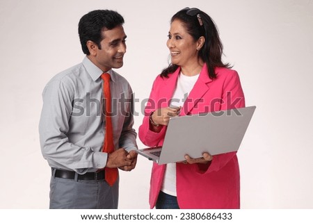 Indian Businessman and businesswoman using a laptop together while standing in grey studio background.