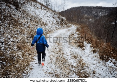 Boy walking on the road rear view, cold weather first snow, child walking alone outside the city, get lost in the forest, road home. High quality photo