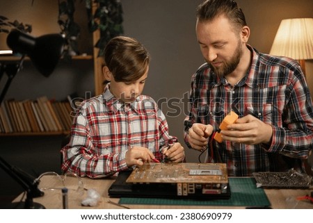 Father and son repairing laptop at home using soldering iron and multimeter to diagnose broken motherboard. Copy space
