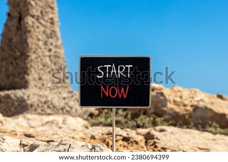 Start now symbol. Concept words Start now on beautiful black chalk blackboard. Beautiful brown stone blue sky background. Business marketing, motivational start now concept. Copy space.