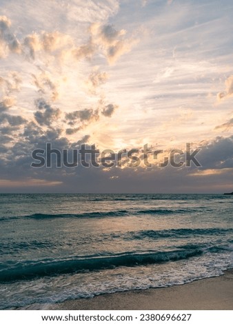 A stunning image of a sunset on the beach of Kish Island, Iran. The sun is setting behind a bank of clouds, casting a warm glow across the sky. 