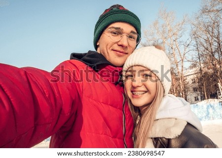 Portrait of a couple of happy teenagers taking photo of yourself, selfie,on a winter day at an outdoor skating rink.Winter entertainment,leisure activity,Valentine's day,generation Z.