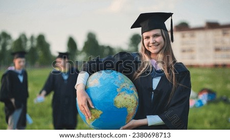 Graduate student girl poses with a globe in a meadow.