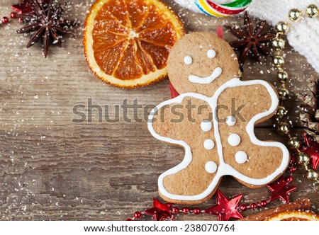 Homemade christmas painted gingerbreads (gingerbread man and red boot) on the wooden background with Christmas decorations and candied orange. Selective focus and place for text. Toned and snow.