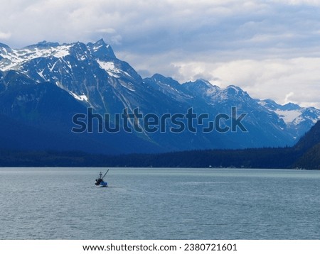 Amidst Haines' breathtaking landscape, a lone fishing boat ventures, juxtaposed against imposing snow-kissed mountains and dense forests. Royalty-Free Stock Photo #2380721601