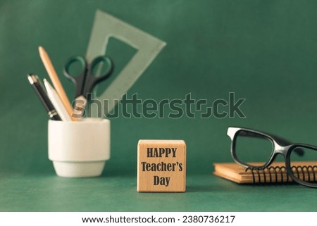 Happy Teacher Day writing on wooden cube front of green board. School and office supplies, stationery accessories. Composition for Teacher's day.