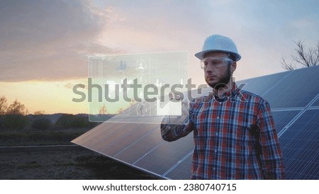 Engineer in front of solar panel works on futuristic table HUD display. Graphics Royalty-Free Stock Photo #2380740715