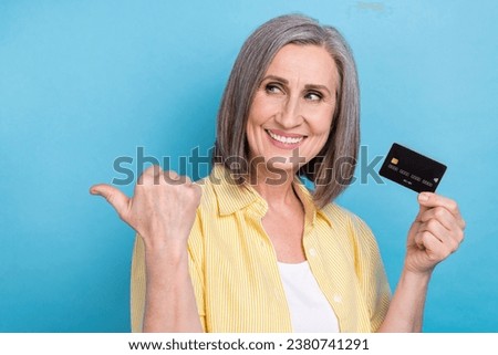 Photo of charming dreamy woman dressed yellow shirt holding bank card thumb empty space isolated blue color background