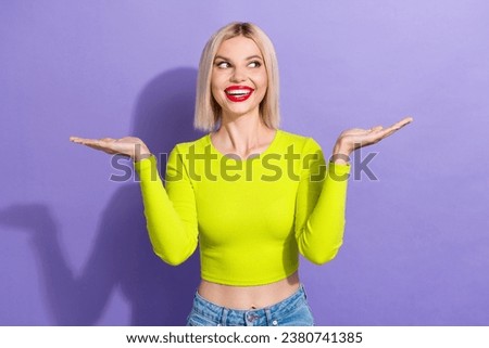 Portrait of funny ecstatic woman dressed yellow top look empty space offer palms demonstrate objects isolated on purple color background