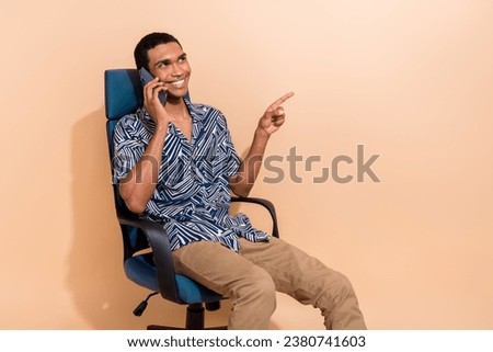 Photo of excited dreamy guy dressed print shirt communicating modern device showing finger empty space isolated beige color background