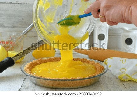 Pouring homemade lemon pie filling into graham cracker crust for a lemon meringue pie in the kitchen