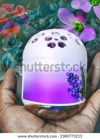 white and purple perfume container in hand. there is a picture of lavender on the container. the background is a picture of various flowers