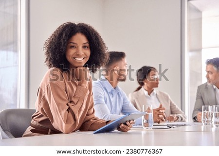 Portrait of happy young African American business woman at diverse team office meeting. Smiling confident professional businesswoman company employee leader with tablet sitting in board room. Royalty-Free Stock Photo #2380776367