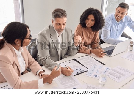 Busy older Latin business man investor checking bank document at office team meeting with financial law experts team thinking of risks managing corporate paperwork. Consultancy advisory services.