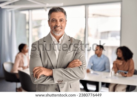 Confident older middle aged Indian business man manager standing at office team meeting. Portrait of elegant smiling professional senior male company executive leader crossing arms in board room. Royalty-Free Stock Photo #2380776449