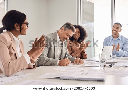Happy old businessman executive investor banker signing legal business document agreement contract at board meeting with attorneys lawyers advisers diverse law team applauding sitting at office table. Royalty-Free Stock Photo #2380776503
