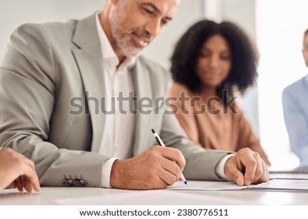 Old senior businessman investor wearing suit signing business legal document. Male bank client writing signature on sales contact making successful investment deal. Focus on hand holding pen. Close up Royalty-Free Stock Photo #2380776511