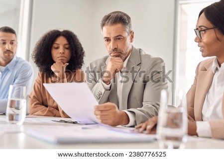 Serious senior Latin business man investor checking bank document at office team meeting with financial law experts lawyers attorneys team thinking of risks. Consultancy advisory services concept. Royalty-Free Stock Photo #2380776525