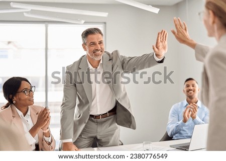 Happy international board executive team leaders partners giving high five celebrating financial success in collaboration, company work achievement over office table at group employees meeting. Royalty-Free Stock Photo #2380776549