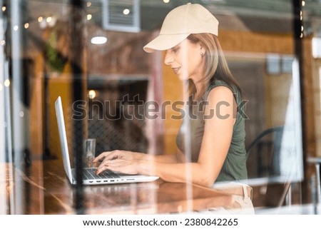 Freelance woman working in a coffee shop with a laptop on her day off. Woman in coffee shop using technology. Photographed through window.Copy space