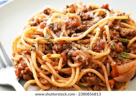 Spaghetti Bolognese with minced beef, onion, chopped tomato, garlic, olive oil, stock cube, tomato puree and Italian herb. Traditional Italian food in white plate with a fork.