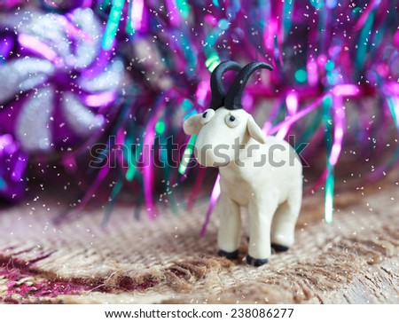 Plasticine world - little homemade white goat with black horns and hooves on purple background with snow, selective focus and place for text