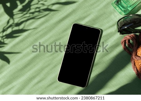 Mobile phone and woman fashion accessory on a green textile background with floral sun light shadow, spring summer feminine stylish brand concept, copy space