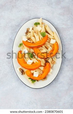 Pasta with baked pumpkins and nuts in a ceramic plate. Tasty autumn food. Top view.