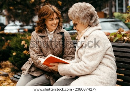 A young woman takes care of an elderly woman in a park against the backdrop of an autumn landscape Royalty-Free Stock Photo #2380874279